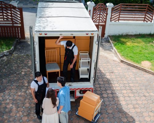 Asian Couple check while unloading boxes and furniture from a pickup truck to a new house with service cargo two men movers worker in uniform lifting boxes. concept of Home moving and delivery.